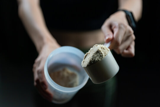 Close up of women with measuring scoop of whey protein and shaker bottle, preparing protein shake.