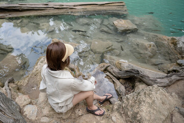Woman sitting on the stone at Erawan waterfall at National Park, Kanchanaburi, Thailand.