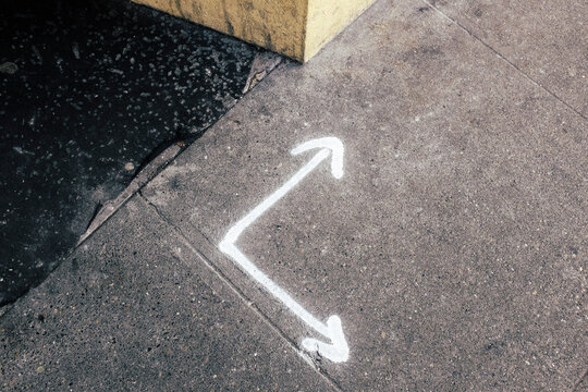 White arrows spray painted on urban sidewalk, corner of building wall in background
