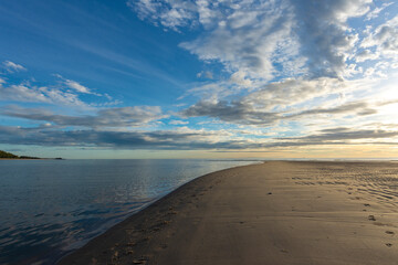 Beautiful sunrise above sea or ocean and small clouds on the sky, reflection of sun in the water and sand on beach