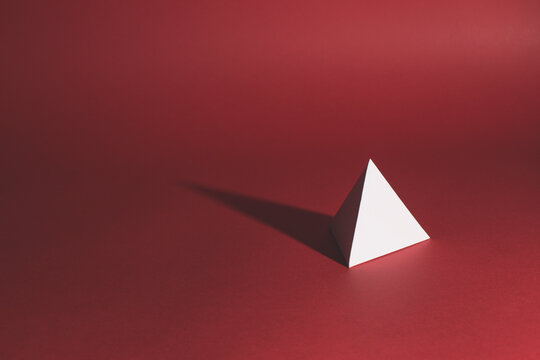 A white paper tetrahedron sits on a red background casting long shadow...