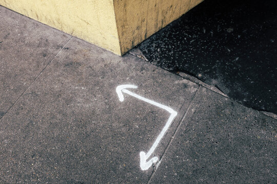 White arrows spray painted on urban sidewalk, corner of building wall in background
