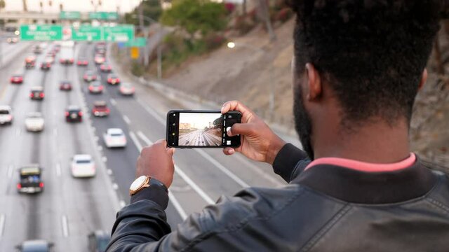 African-American man takes photos of the morning traffic with his smartphone in Los Angeles