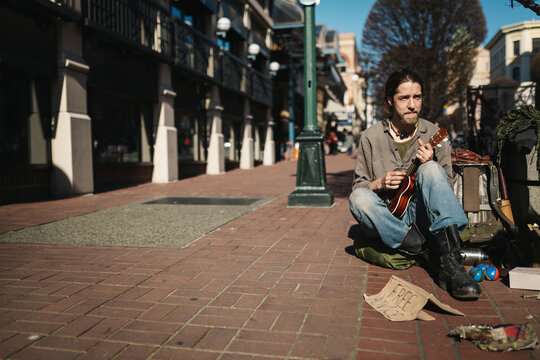 Portrait of young homeless man panhandling on the sidewalk - playing music