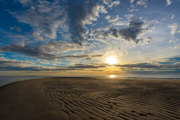 Beautiful sunrise above sea or ocean and small clouds on the sky, reflection of sun in the water and sand on beach