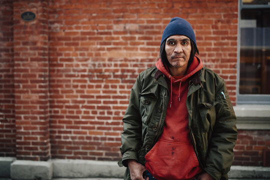 Portrait of older, native homeless man standing by brick wall