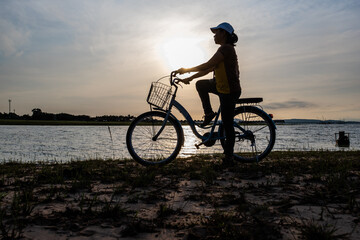 Silhouette of women with vintage bicycle near the beach during sunrise.