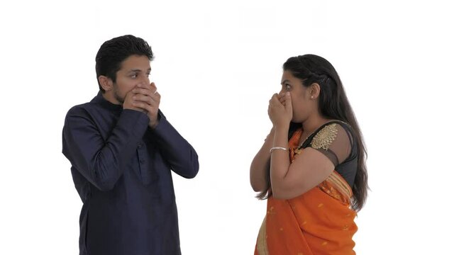 Young indian couple covering mouth with both hands with sorrowful look because of bad news. Isolated on white background.