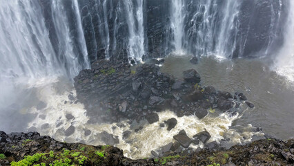 Powerful streams of Victoria Falls fall into the gorge. At the bottom are black stones. The water...