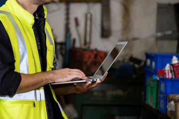 Confident of engineer or worker wearing a safety jacket and typing keyboard on the laptop which shown back screen. Working in manufacturing, Many tools, and spray bottles. Industrial concept
