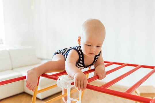 Cute baby performs gymnastic exercises on a wooden home sports complex stairs and rings. Children's sports exercises. Physical education of children at home