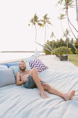 A young caucasian man laying on a day bed at sunset by the beach.