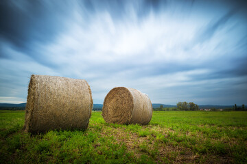 Hayrolls on a field with dramatic clouds long exposure