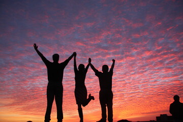 People with their arms raised in celebration with a vibrant, pink sky
