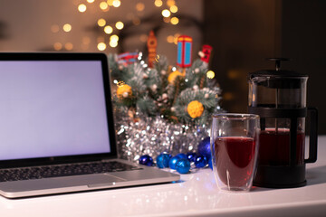 Laptop with white screen next to french press and tea near new years decorations. christmas theme template.