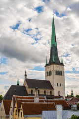 Fototapeta na wymiar St. Olav's Church (Oleviste kirik) and the roofs of old town houses in Tallinn, Estonia. Cloudy summer day