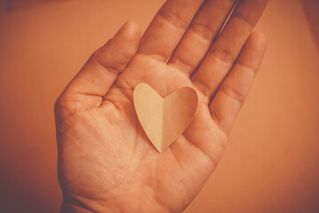 Eine Hand hält ein ausgeschnittenes Herz aus Papier. Ton in Ton. Hautfarben.