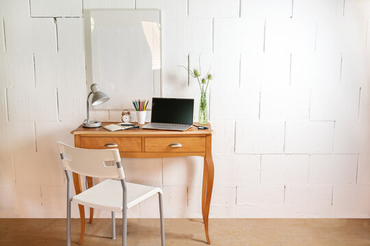 Small Wooden Table And Chair As A Tiny Place For A Home Office With Laptop, Desk Lamp And Tools Against A Rough White Wall, Copy Space,