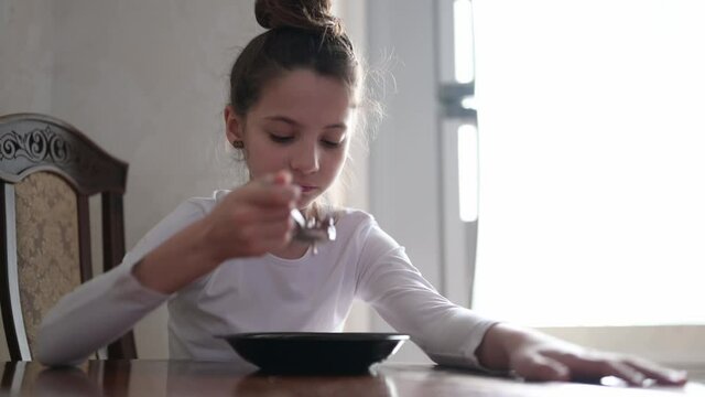 one little caucasian girl eating from dish using spoon at home bright kitchen at morning