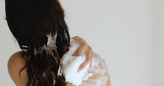 Close up rear back view wet millennial female holding bath sponge lathers her slender body using soap or shower gel product. Keep personal hygiene, body care, start new day everyday routine concept