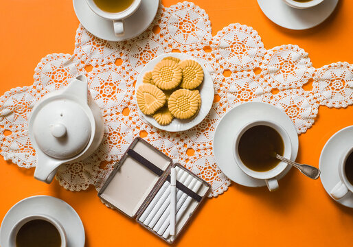 Coffee cups with cookies on tablecloth on orange background / ook from above