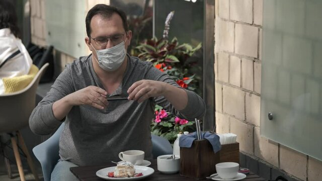 Man have couh in medical mask doing food photo on a mobile phone during a pandemic