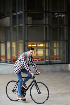 Young man riding a bike nearby a building in the campus