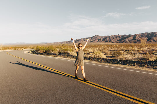 Pregnant Blonde Woman Walking In Middle Of Desert Highway With Arms Raised In Happiness