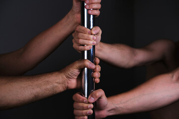 Four hands holding a pole dance bar. Dark background.