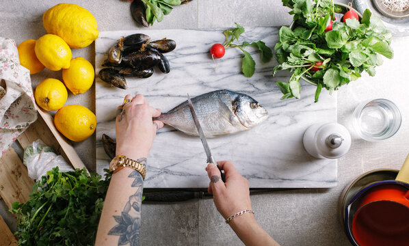 Woman preparing seabream and mussels for cooking on her kitchen table.