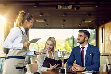 Business couple talking to waitress while choosing order from a menu in a restaurant.