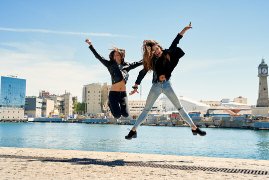 Two cheerful girlfriends jumping at pier