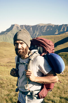 Portrait of a bearded male with his back pack surrounded by mountains.
