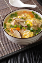 Japanese Zosui rice soup with egg, mushrooms, vegetables and chicken meat close-up in a bowl on the table. vertical