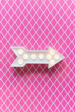 Arrow marquee light on a pink background.