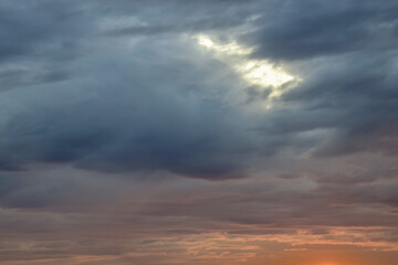 Dusky stormy sunset, dramatic sky in orange and gray colors. Natural background. Rays of light shining through dark clouds.