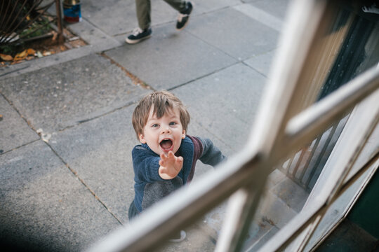 Young toddler waving enthusiastically through a window.
