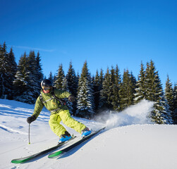 Young man backpacker skiing up and down slopes. Male skier training and having fun in sunny winter day. Backcountry skiing concept. Fir trees and clear blue sky with copy space on background.