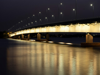 A beautiful night cityscape of an illuminated highway bridge casting reflections on the water.