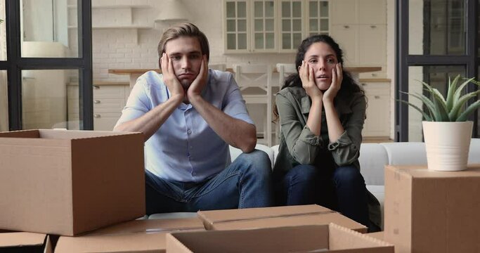 Tired couple sit on sofa surrounded by heap of big carton boxes look at each other feels upset due long run house remodeling, renovations, repairs. physical exhaustion after move out from flat concept