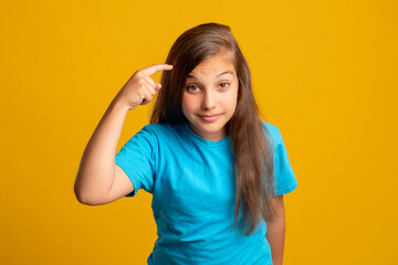 Think use your brain. Smart child. Creative idea. Memory knowledge. Portrait of sarcastic young girl in blue t-shirt pointing finger at temple looking at camera isolated on orange background.