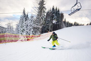 Male skier skiing and carving turn on prepared ski slope at ski resort after taking chairlift on...