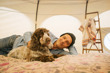 Glamping - Caucasian Man Stroking Cocker Spaniel on Bed Inside Large Circular Tent