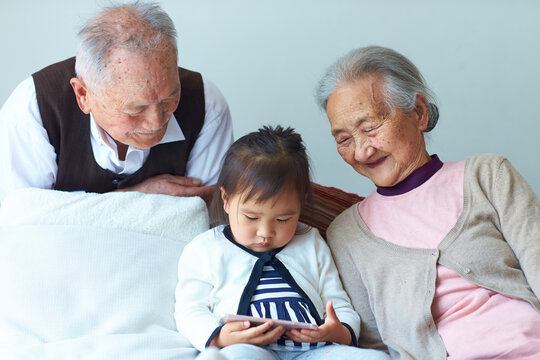 great grandparents watching their great granddaughter playing smart phone