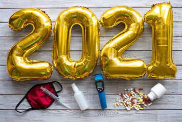 Number 2021 made from golden inflated balloons on a rustic wooden table along with coronavirus...