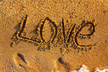 The word love is written on the sandy seashore.