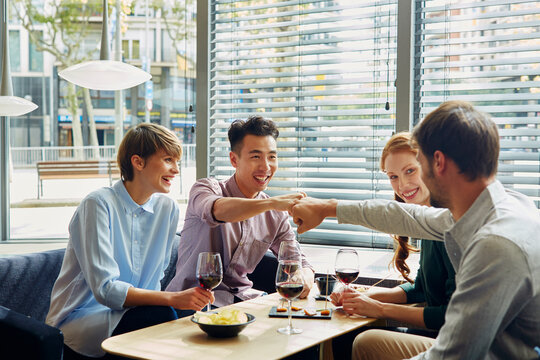 Women Looking At Friends Doing Fist Bump In Restaurant