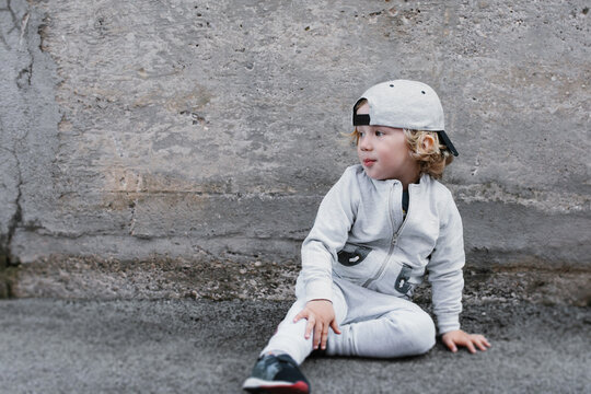 Cute boy in backward hat sitting near wall