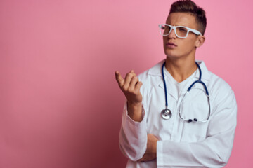 male doctor in a medical gown with a stethoscope around his neck on a pink background and glasses on his face