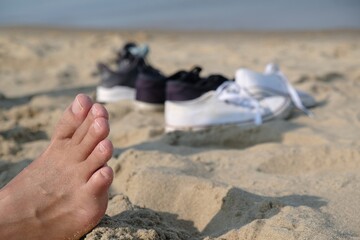 A man's naked foot is covered with sand on a beach by the sea. Taking care of the health of the feet and protection against mycosis.